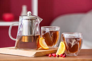Teapot, glasses with hot tea, orange and cranberry on table in room