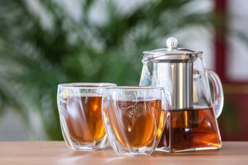 Teapot and glasses with hot tea on table in room