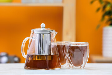 Teapot and glasses with hot tea on table in kitchen