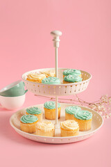 Dessert stand with tasty cupcakes, cups and flowers on color background