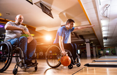 Obraz na płótnie Canvas Two young disabled men in wheelchairs playing bowling in the club