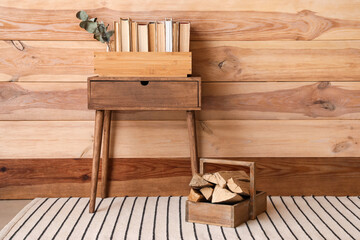Table with books and firewood near wooden wall