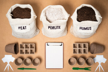 Peat moss, perlite and worm humus as potting soil mix in rustic fabric bags with a seed starting kit, peat pots, plant labels and a clipboard to take notes on a brown mdf surface. - obrazy, fototapety, plakaty
