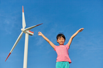 夏の海の海岸で元気で遊んでいる女の子の子供と風力発電の様子