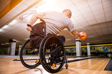 Young disabled man in wheelchair playing bowling in the club
