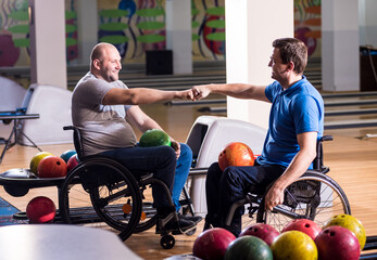 Two young disabled men in wheelchairs playing bowling in the club - obrazy, fototapety, plakaty