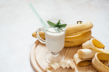 Milk banana shake decorated with mint leaves in a latte glass with handle on light background with...