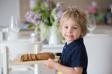 Child, blond toddler boy, holding wooden cutting board with homemade corn bread, serving at home