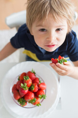 Blond toddler child, holding a bowl with strawberries, looking up at the camera
