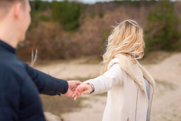 Follow me. Romantic concept. Young caucasian woman with long blonde hair outdoors holding guy's hand.Traveling together.