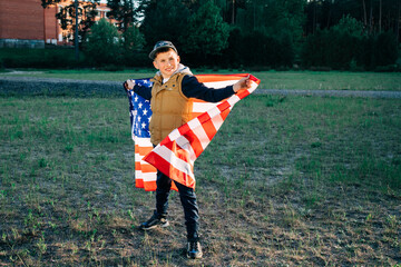 Extremely happy satisfied boy with  holding in hands big american flag sincerely rejoicing. Green...