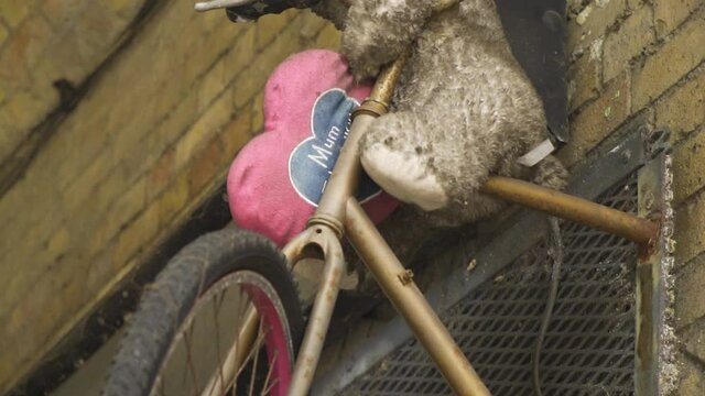 dirty teddy bear left alone on a bike mounted creatively on the wall with pink heart pillow saying mum emotional childhood memories abandoned left alone grown up without inner child slow motion