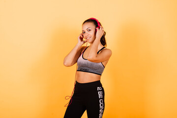 Confident young fit african sportswoman listening to music with headphones over yellow background