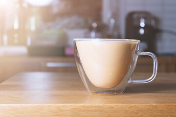 Glass mug of homemade cappuccino on rustic wooden table in country house on early sunny morning. 