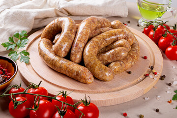 Raw meat sausages from beef and minced pork on round wooden cutting board and products for cooking it close up
