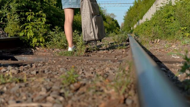 A woman with a suitcase in her hand walks along the sleepers. Travel on railroad tracks. Old train track