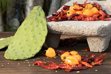 Close-up of beautiful habanero peppers surrounded by chili seeds with a background of Mexican pre-Hispanic foods such as nopales and various chili peppers and served with a traditional Mexican Metate