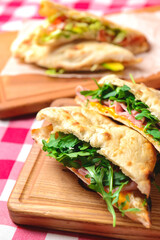 Ham and fresh vegetables in pita bread on wooden table with red plaid tablecloth.