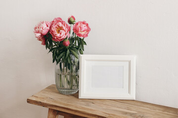 Floral still life scene. Pink peonies flowers, bouquet in glass vase on wooden table. White horizontal picture frame mockup. Wedding, birthday celeberation concept. Lifestyle photo