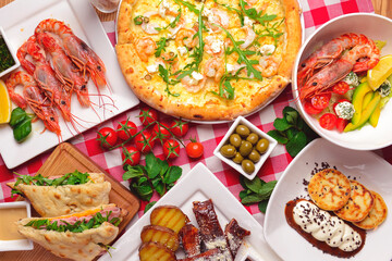 Traditional Italian cuisine concept flat lay. Sea food pizza, cooked shrimps, caramel ribs, ham pita sandwich.