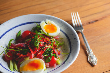 Tuna salad with vegetables, boiled eggs, cherry tomatoes and spices over wooden background.