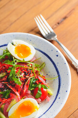 Tuna salad with vegetables, boiled eggs, cherry tomatoes and spices over wooden background.