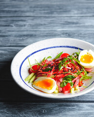 Tuna salad with vegetables, boiled eggs, cherry tomatoes and spices over wooden background.