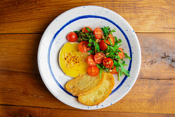 Baked camambert cheese with jam and fresh vegetable salad made from cherry tomatoes and green arugula