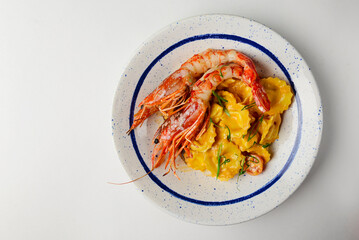 Italian ravioli with big cooked shrimps served on a white plate over white background.