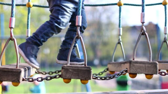 child's kid's legs in blue jeans and boots passing obstacle course attraction in playground