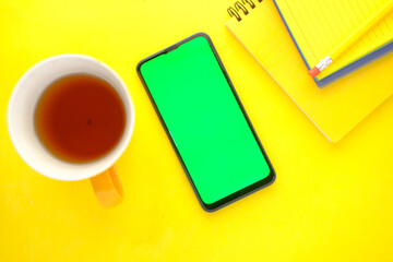 top view of smart phone, coffee mug and notepad on yellow background 
