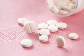Close up of many while color medical pills spilling on pink 