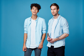 curly guy in a shirt stands next to a young man in a t-shirt on a blue background cropped view