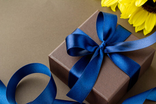 鮮やかな青いリボンで結んだ茶色の箱とひまわりの花とこげ茶色の背景のプレゼントのイメージ