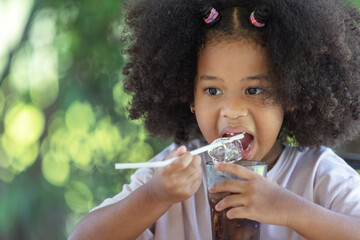 Childhood and healthy eating concept - little African American curly hair girl eating ice from soft...