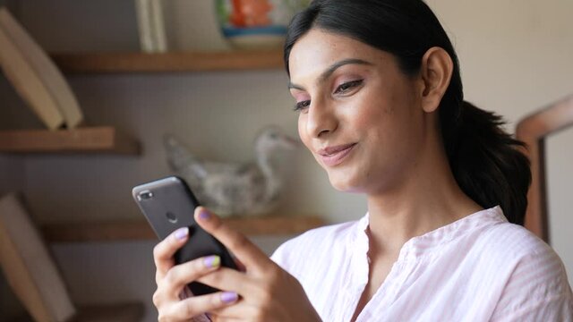 Beautiful Asian woman smiling happily while doing chat reading message on her smart phone at home indoor.lifestyle concept.cheerful Asian girl happily chatting online with friends on smart phone.