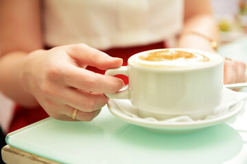The girl's hand holds a cup of coffee standing on the table. - 435357507