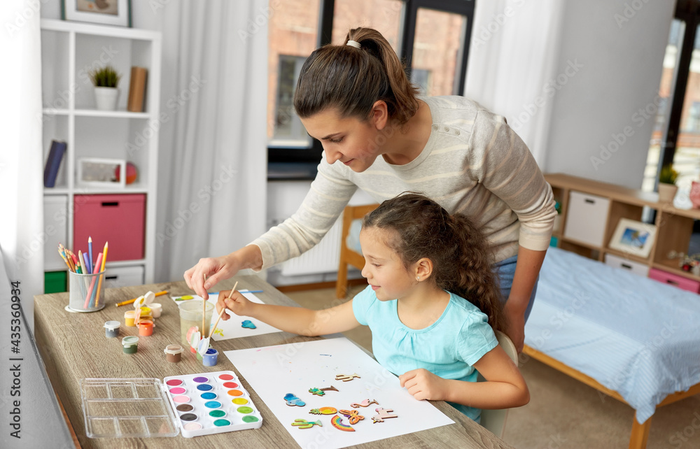 Poster family, motherhood and leisure concept - mother spending time with her little daughter drawing or painting wooden chipboard items with colors at home