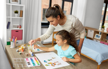 family, motherhood and leisure concept - mother spending time with her little daughter drawing or...