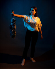 Girl in white shirt with dust brush on a dark background with colored light