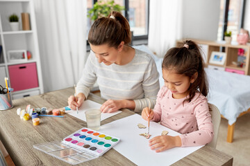 family, motherhood and leisure concept - mother spending time with her little daughter with colors painting chipboard items at home
