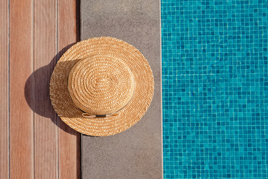 Woman's straw hat lying on the edge of the swimming pool with blue water