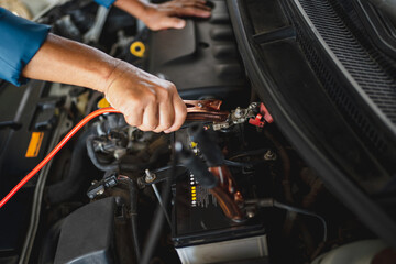 Car mechanic uses a battery jumper cable to charge the dead battery. Car repair service concept.