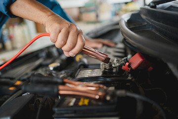Close-up hands of a car mechanic holding the battery jumper wire. He uses battery jumper cables to charge a dead battery.