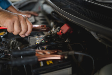 Fototapeta premium Close up of hand Charging car battery with electricity trough jumper cables.