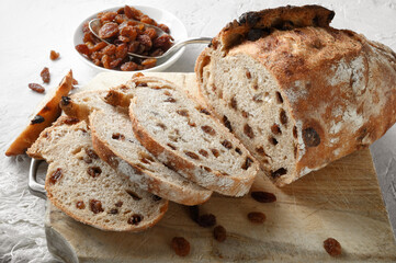 Raisin bread, traditional loaf of sliced bread with cutting board and rustic white plaster background, closeup.