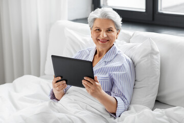 technology, old age and people concept - senior woman with tablet pc computer in bed at home bedroom