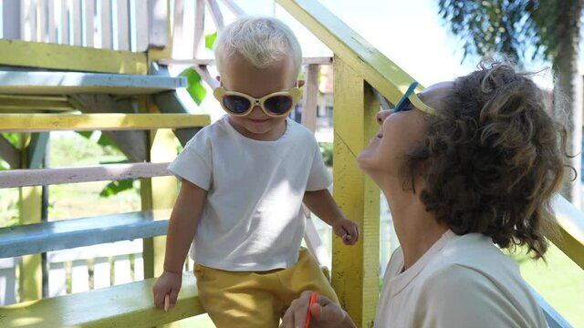 Young Caucasian mother gives a kiss to her 2 years old baby daughter on a playground