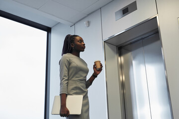 Minimal portrait of African-American businesswoman waiting for elevator in office building and...