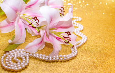 White lilies and pearl necklace on a shiny gold background
